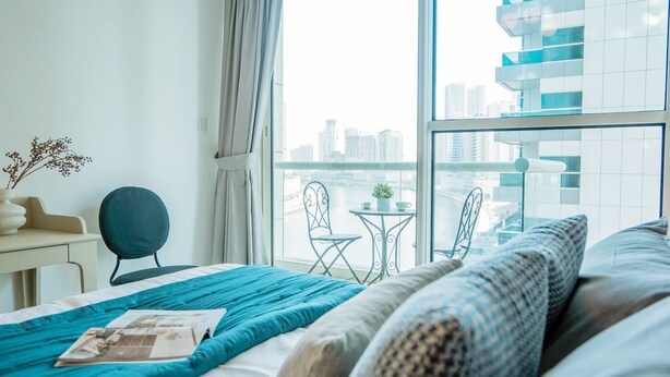 Ein modernes Hotelzimmer mit großem Fenster, einem Bett mit blauer Bettwäsche, einem Schreibtisch mit Stuhl und einem kleinen Balkon.
