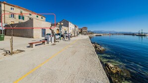 A coastal street with buildings, a sandy path, and a calm sea. - A1 - spacious apt on the seafront with terrace (Kaštel Stari)