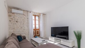 A modern living room with a stone wall, a large flat-screen TV, a sofa, a coffee table, and a potted plant. - A1 - spacious apt on the seafront with terrace (Kaštel Stari)