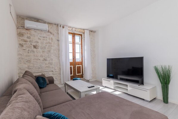 A modern living room with a stone wall, a large flat-screen TV, a sofa, a coffee table, and a potted plant.