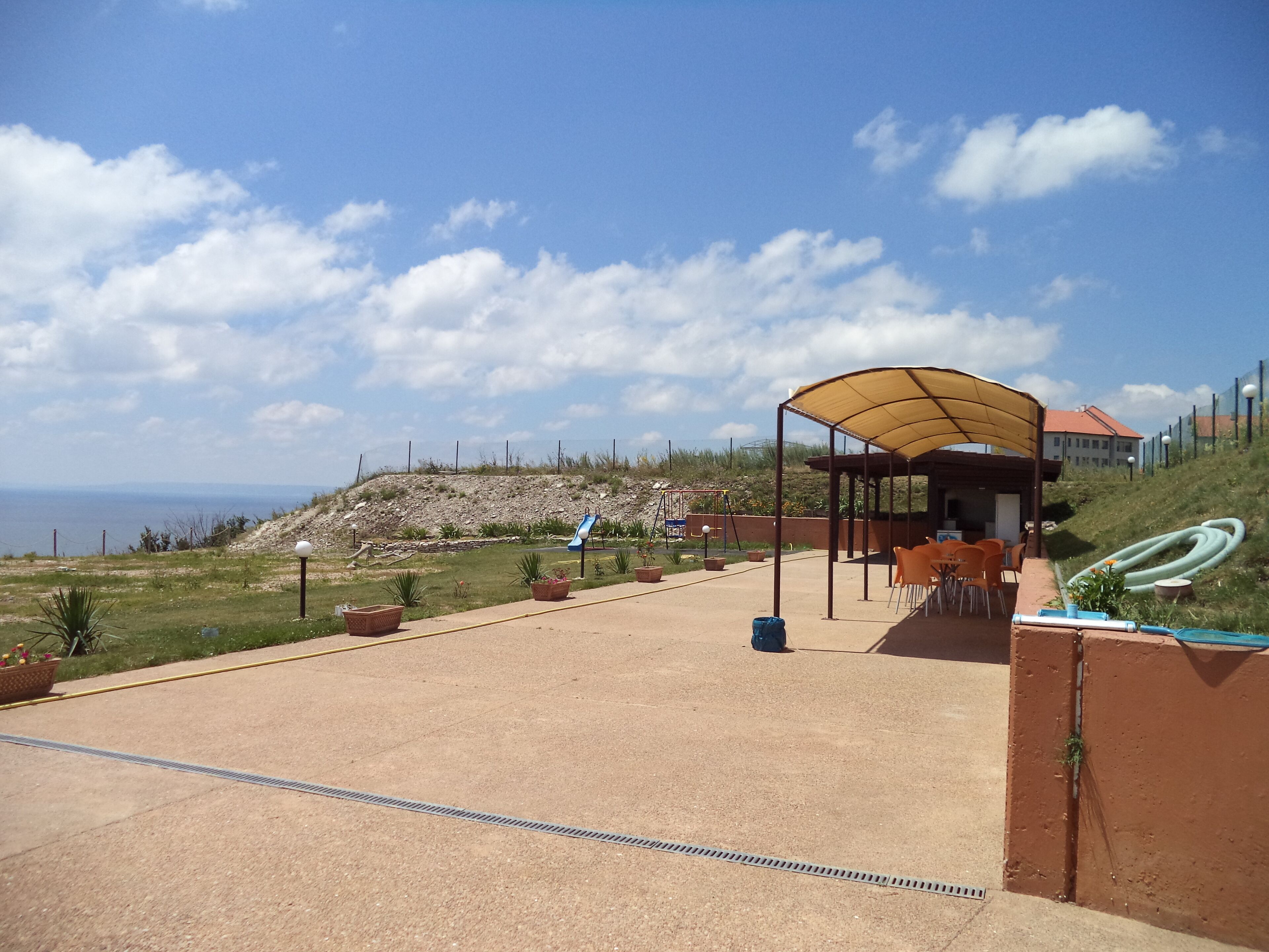 Un espace extérieur abrité, aménagé avec des sièges, un terrain de jeux avec un toboggan et une vue sur la mer.