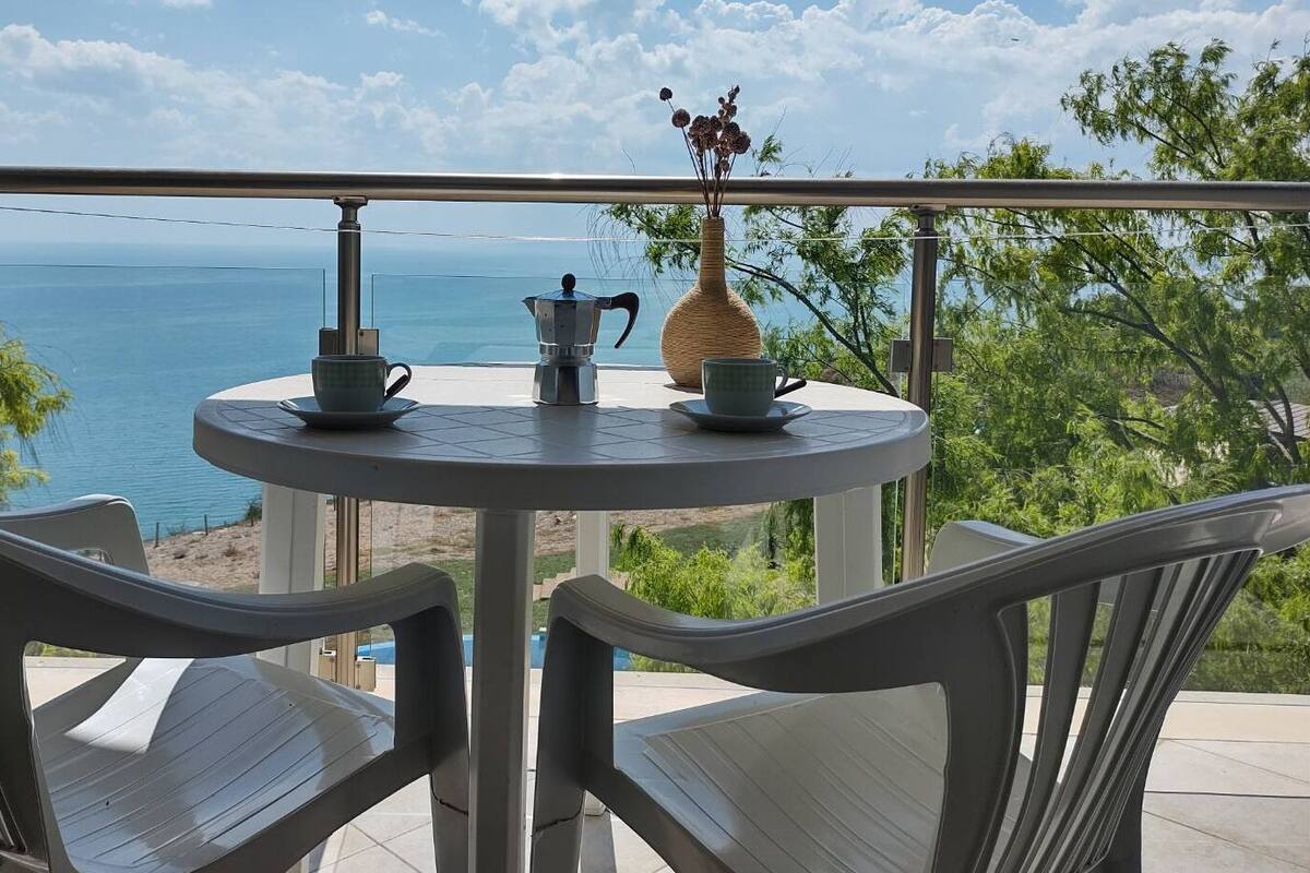 A round table with two chairs on a balcony overlooking a beach.