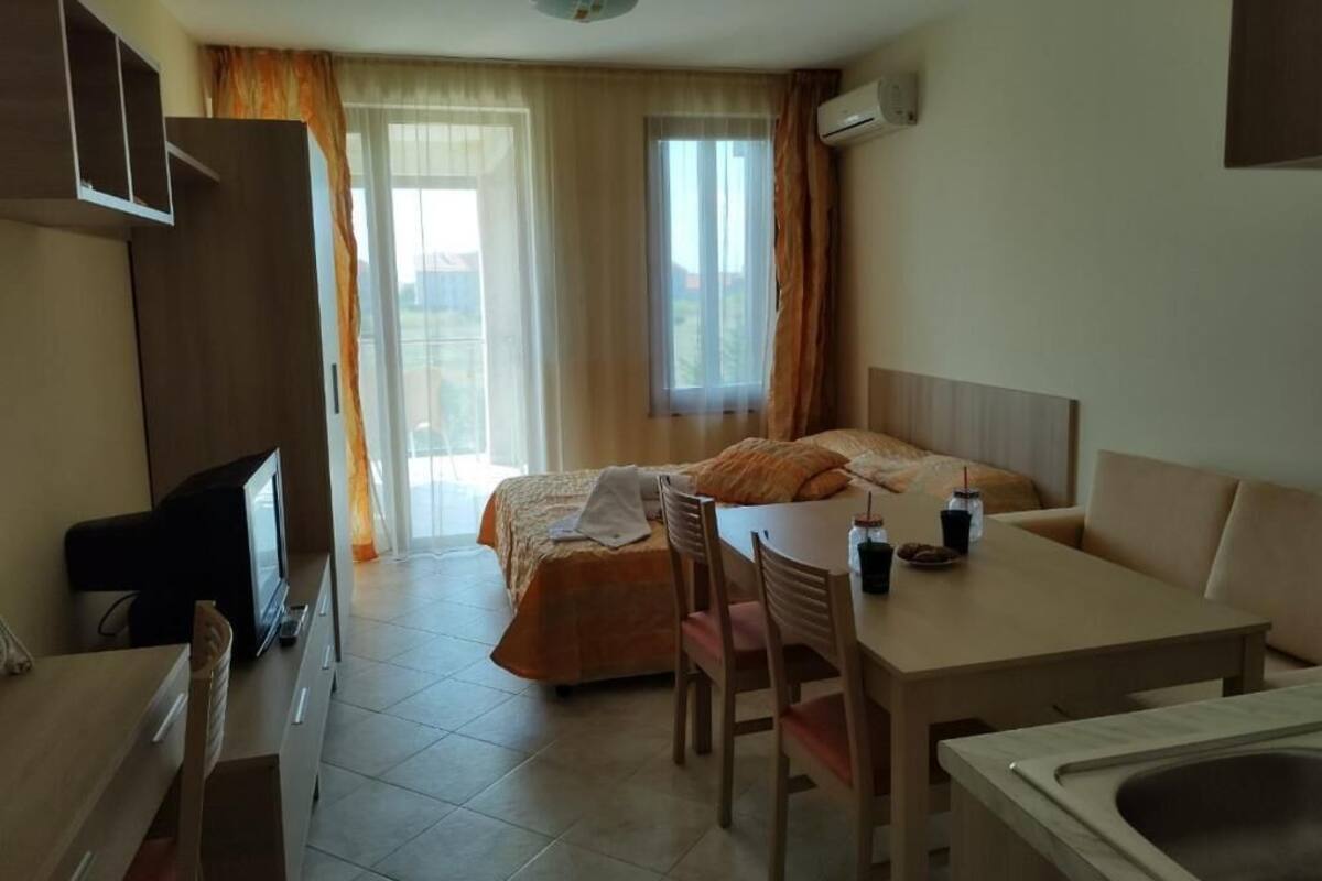 A hotel room with a bed, a desk with a chair, a television, and a window with curtains.