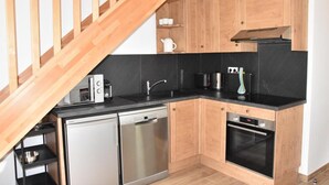 A compact kitchen with wooden cabinets, a black countertop, a dishwasher, a stove, and a wooden staircase. - 250m from resort center, 1st floor, balcony, parking, tv, ski locker, 60m², Pralognan-la-Vanoise (Pralognan-la-Vanoise)