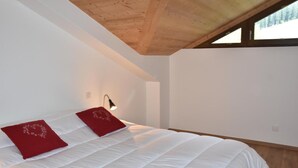 A bedroom with a wooden ceiling, white walls, and a large bed with red pillows. - 250m from resort center, 1st floor, balcony, fireplace or stove, parking, tv, ski locker, 67m² (Pralognan-la-Vanoise)