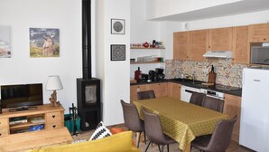 A compact living space with a sofa, TV, and a fireplace. It includes a dining area with a table and chairs, and a kitchen with cabinets and appliances. - 250m from resort center, 1st floor, balcony, fireplace or stove, parking, tv, ski locker, 67m² (Pralognan-la-Vanoise)
