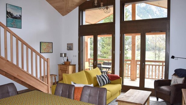 A spacious living area with a yellow sofa, a wooden dining table, and a staircase. - 250m from resort center, 1st floor, balcony, fireplace or stove, parking, tv, ski locker, 67m² (Pralognan-la-Vanoise)