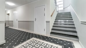 A hallway with a tiled floor, a staircase with a handrail, and a door. - MARGI Maya Apartments (Szczecin)
