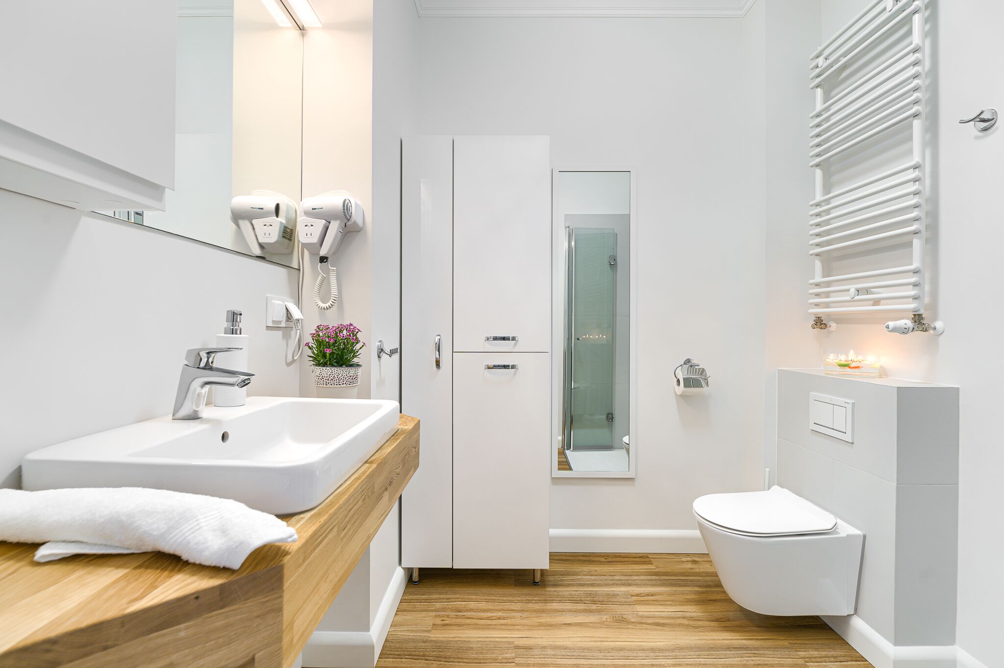 Een moderne badkamer met een wit wastafel, houten badkamerkastje, haardroger en een douchecabine van glas.