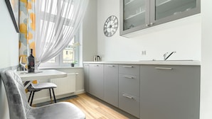 A modern kitchen with grey cabinets, a white countertop, a stainless steel sink, and a window with sheer curtains. - MARGI Maya Apartments (Szczecin)