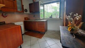 Une cuisine avec des meubles de rangement en bois, une fenêtre donnant sur des arbres, un évier et une table en bois sur laquelle est posé un vase de fleurs.