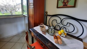 Une pièce avec une table en bois, un cadre de lit en métal, une fenêtre et une œuvre d’art florale encadrée accrochée au mur.