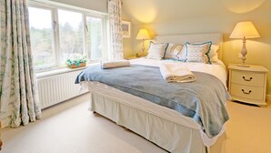 Un dormitorio ordenado con una cama grande, dos mesitas de noche con lámparas, una ventana con cortinas y un radiador.