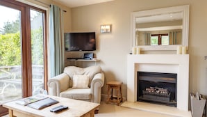 Una sala de estar con chimenea, televisor, sofá y una mesa con controles remotos.