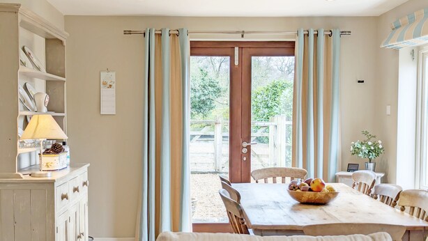 Un comedor con una mesa lista para cuatro personas, un sofá y una zona de cocina con armarios y una lámpara.