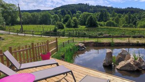A wooden deck with lounge chairs and a table, overlooking a pond and a forested hillside. - Gîte l'Oule near Thiers - 4 people in Viscomtat (Viscomtat)