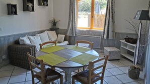 A dining area with a round table, chairs, a sofa, and a window with curtains. - Gîte l'Oule near Thiers - 4 people in Viscomtat (Viscomtat)
