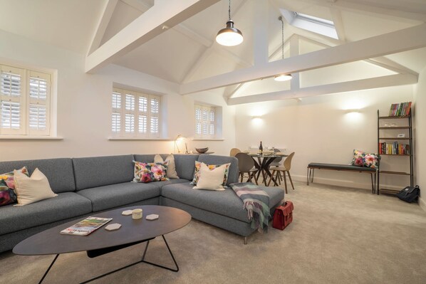 Ein modernes Wohnzimmer mit einem grauen Ecksofa, einem Couchtisch und einem Essbereich mit Tisch und Stühlen.