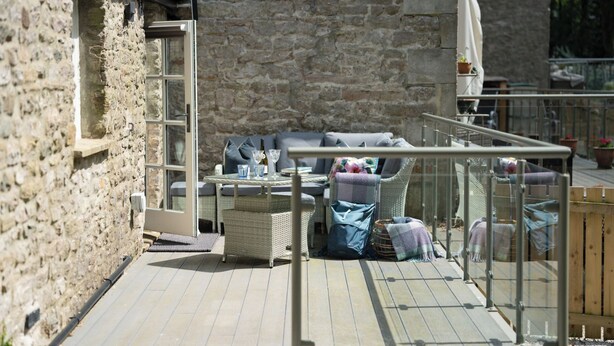A stone building with a patio area featuring wicker furniture, a table with drinks, and a view of the surrounding area. - Contemporary Home Nr Kirkby Lonsdale - Spacious Garden (Carnforth)
