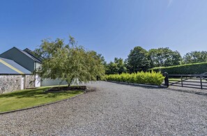 A gravel driveway leading to a building with a stone facade and a tree in the center.