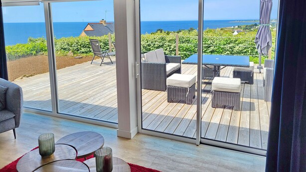 Ein Zimmer mit einer großen Schiebeglastür, die auf eine Terrasse mit Meerblick führt.