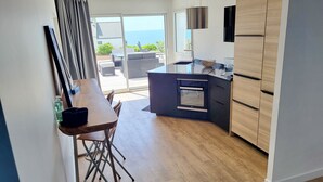 Eine moderne Küche mit Einbauofen, ein Essbereich mit Tisch und Stühlen sowie Meerblick durch große Fenster.