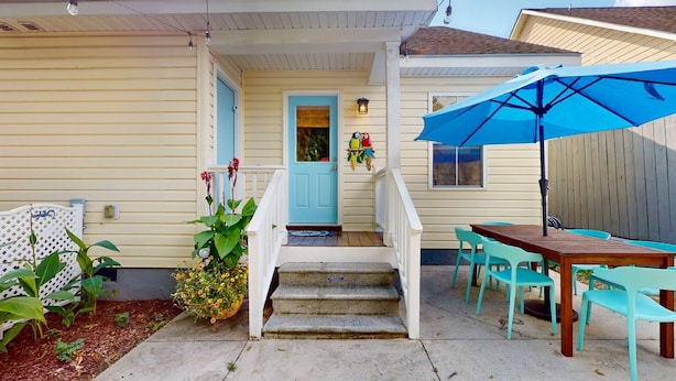 A house with a porch, a blue door, a staircase, a dining table with chairs, and a blue umbrella. - Mins to Downtown, Live Oak Concerts, Convention Center & Beach! Pet Friendly!! (Wilmington)