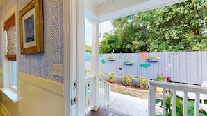 A porch with a white railing, a wooden fence with colorful decorations, and a garden with various plants. - Mins to Downtown, Live Oak Concerts, Convention Center & Beach! Pet Friendly!! (Wilmington)