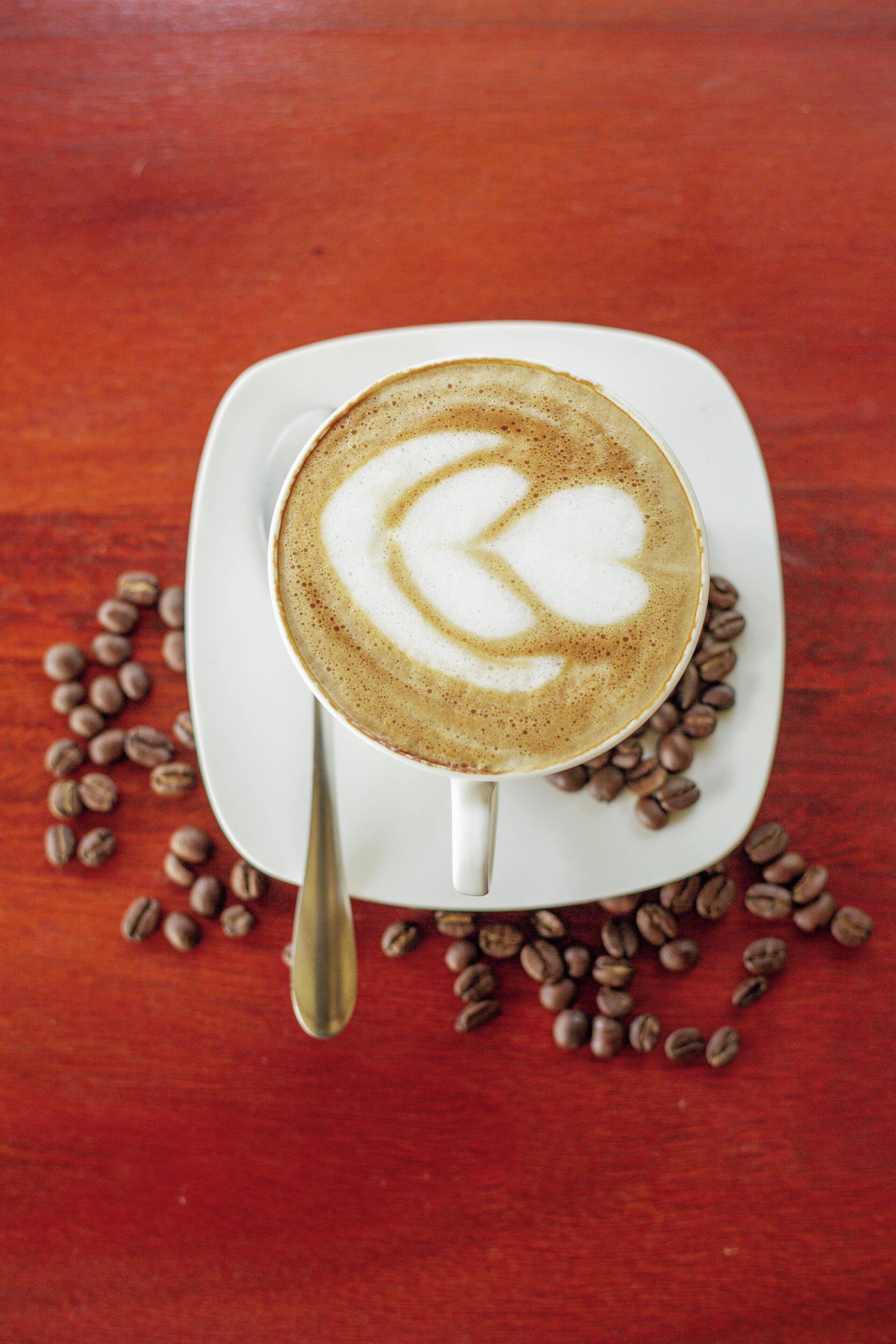A cup of coffee with latte art on a white plate, surrounded by coffee beans on a wooden table.