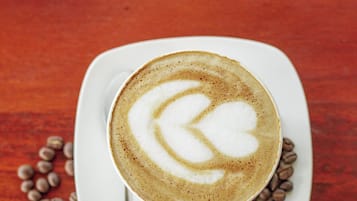 A cup of coffee with latte art on a white plate, surrounded by coffee beans on a wooden table.