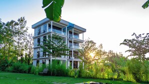 A multi-story building with balconies, surrounded by lush greenery and a well-maintained lawn. - Shose Farmhouse Chalets & Campsite (Moshi)