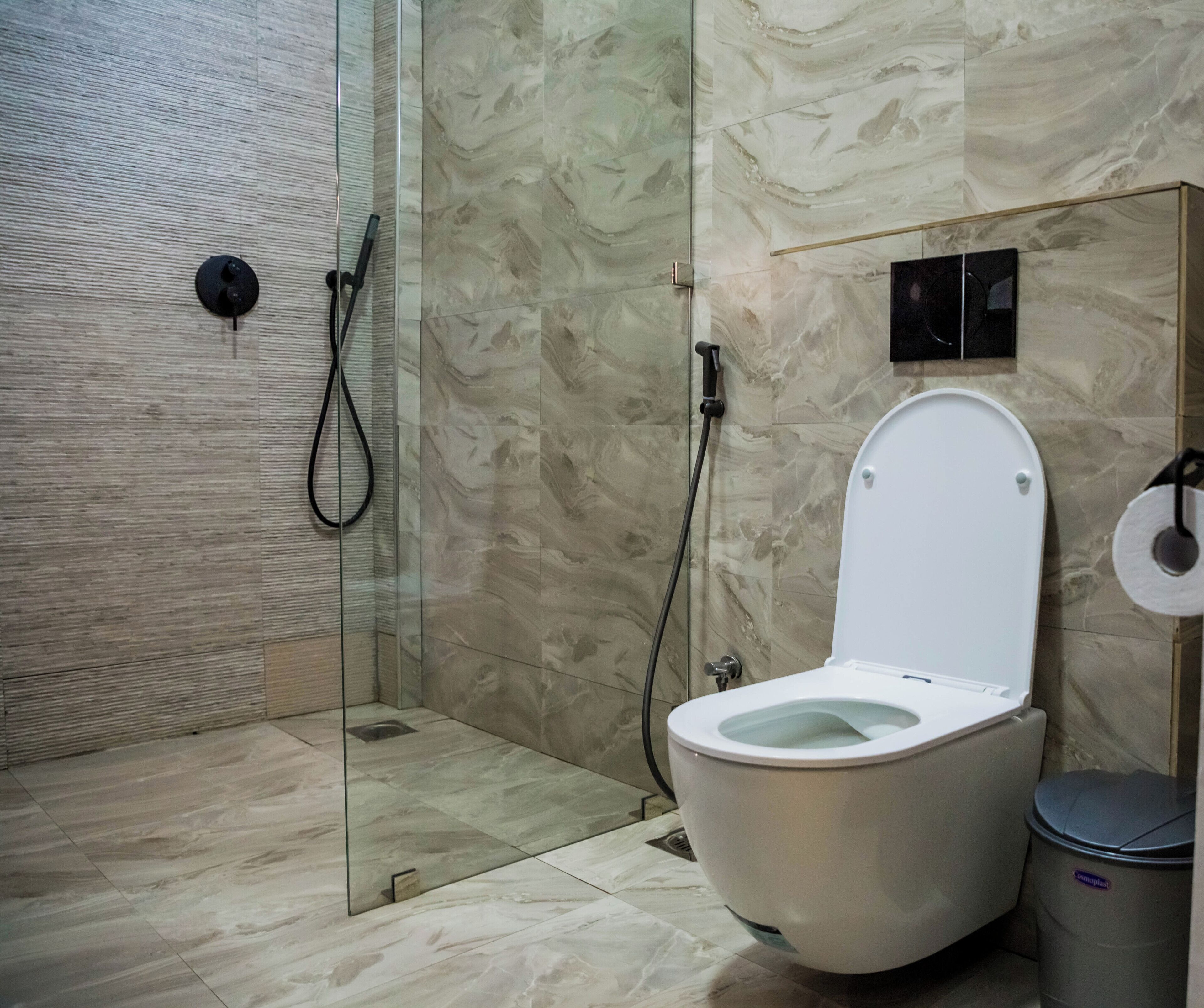 A modern bathroom with a glass-enclosed shower, a white toilet, and a trash bin.