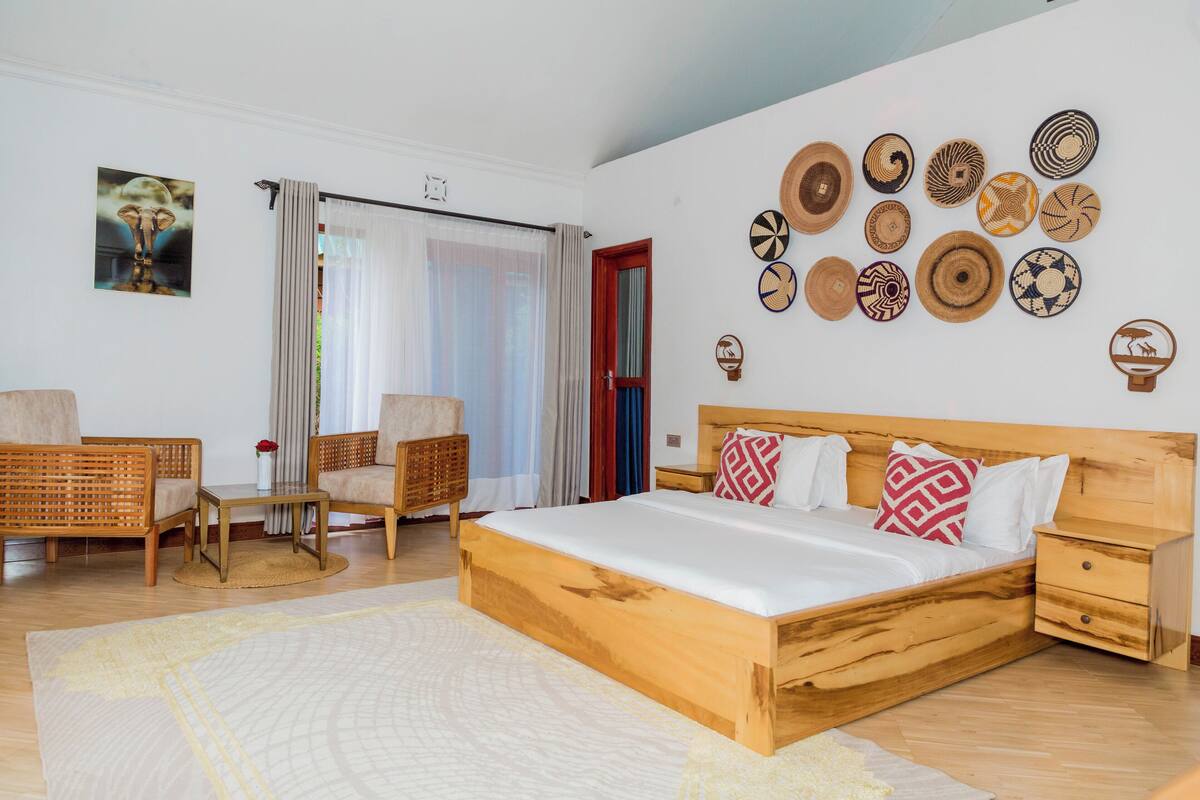 A bedroom with a wooden bed, two wicker chairs, a small table, and a wall decorated with various woven plates.