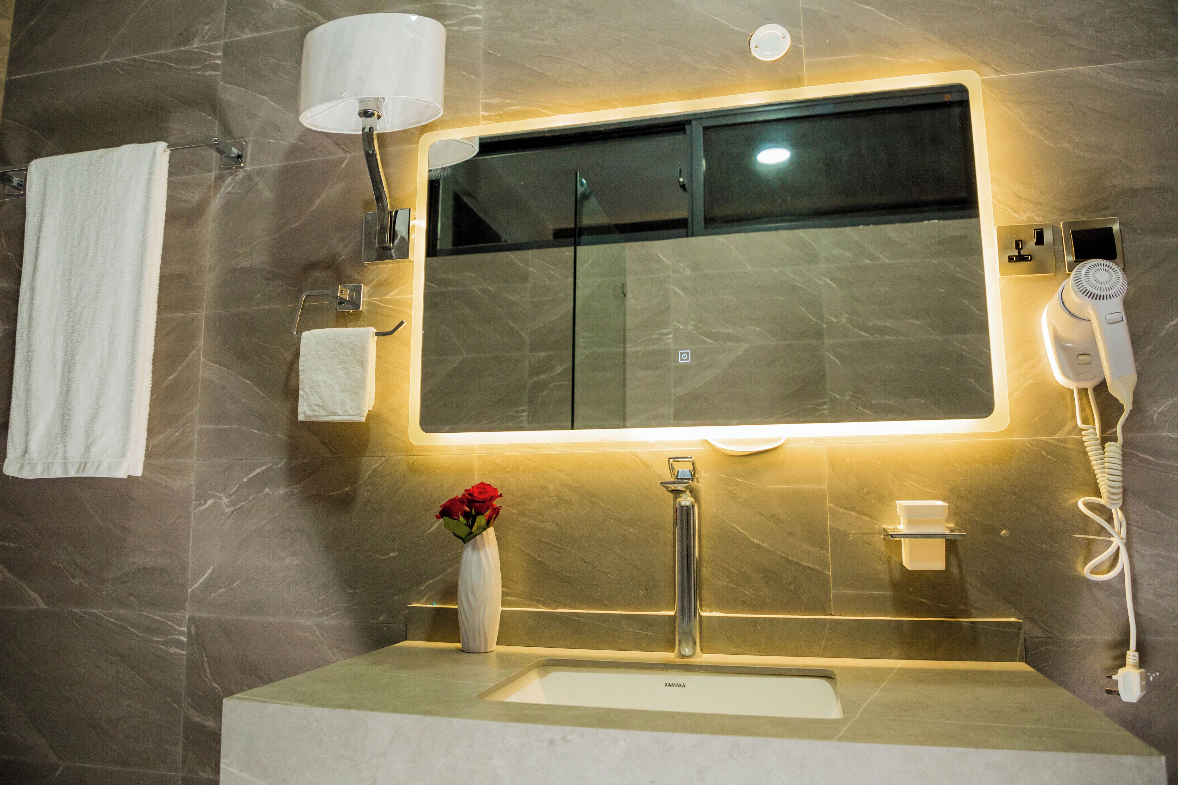 A bathroom with a large mirror, a sink, a towel rack, a vase with flowers, and a hairdryer.