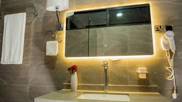 A bathroom with a large mirror, a sink, a towel rack, a vase with flowers, and a hairdryer.