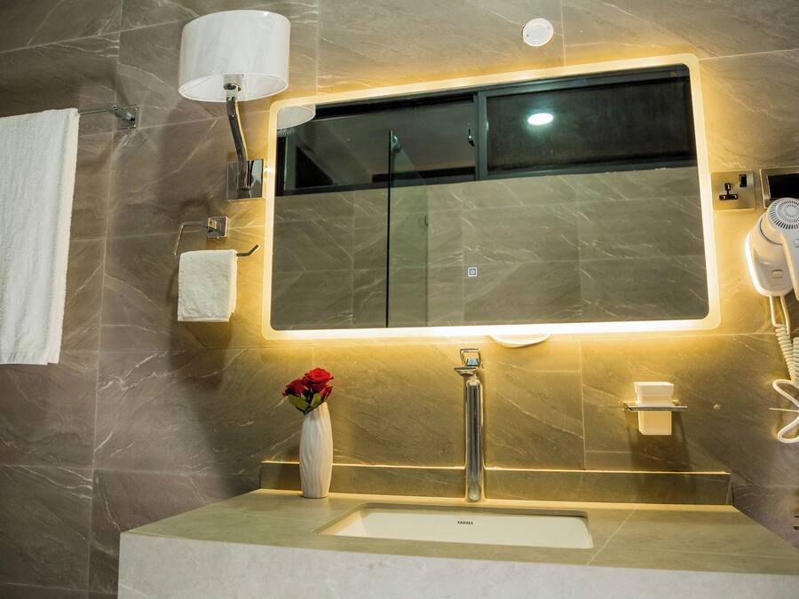 A bathroom with a large mirror, a sink, a towel rack, a vase with flowers, and a hairdryer.