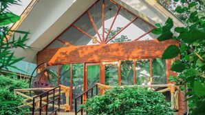 A modern building with a sloped roof, a wooden staircase leading to a covered porch, and a surrounding lush garden. - Shose Farmhouse Chalets & Campsite (Moshi)