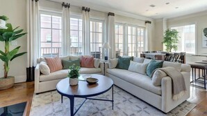 En moderne stue med to sofaer, et sofabord og store vinduer med gardiner.