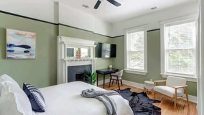 Une chambre avec un lit, un bureau, une chaise, une cheminée et un téléviseur.