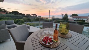 A terrace with a table set for two, featuring a bottle of wine, two glasses, and a plate of strawberries.