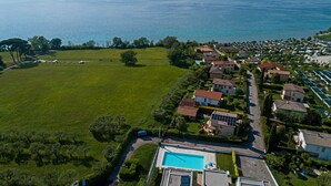 An aerial view of a coastal residential area with houses, a large green field, and a swimming pool.