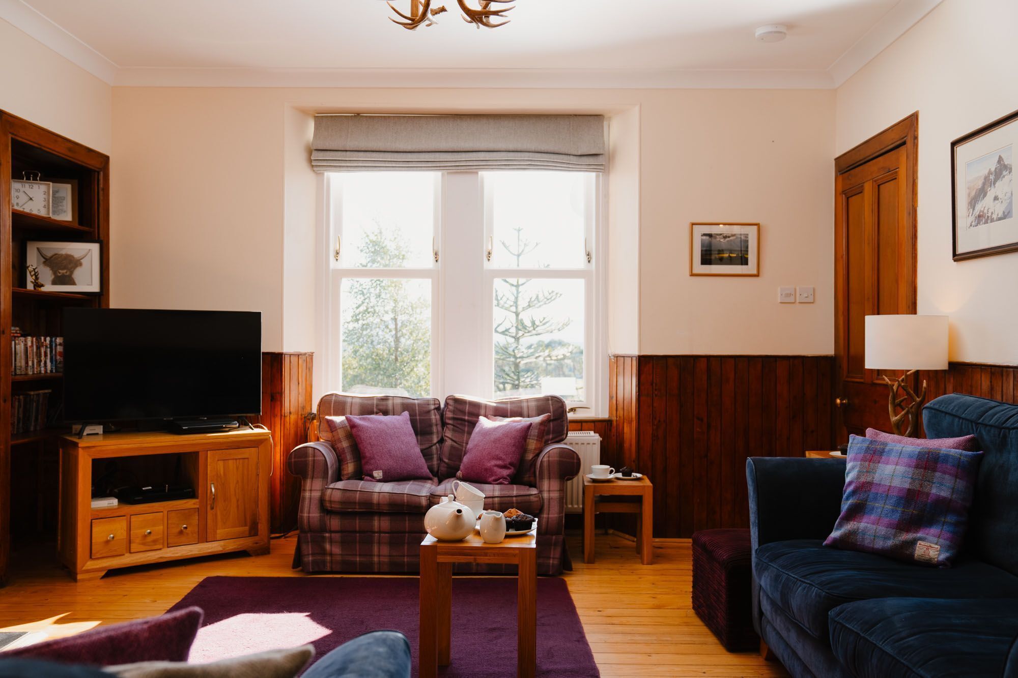 Una sala de estar acogedora con televisión, dos sofás, una mesa de centro y una ventana con vista a árboles.