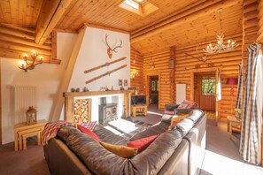 A log cabin interior with a fireplace, a sofa, a television, and a chandelier.