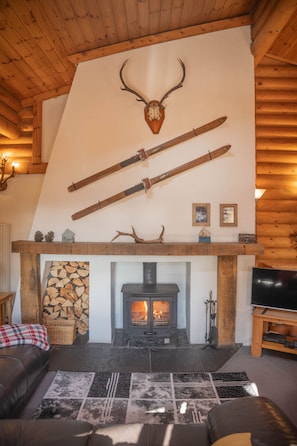A cozy living room with a fireplace, wooden beams, and antlers on the wall. - Beaver Creek Lodge -  a lodge that sleeps 8 guests  in 3 bedrooms (Aviemore)
