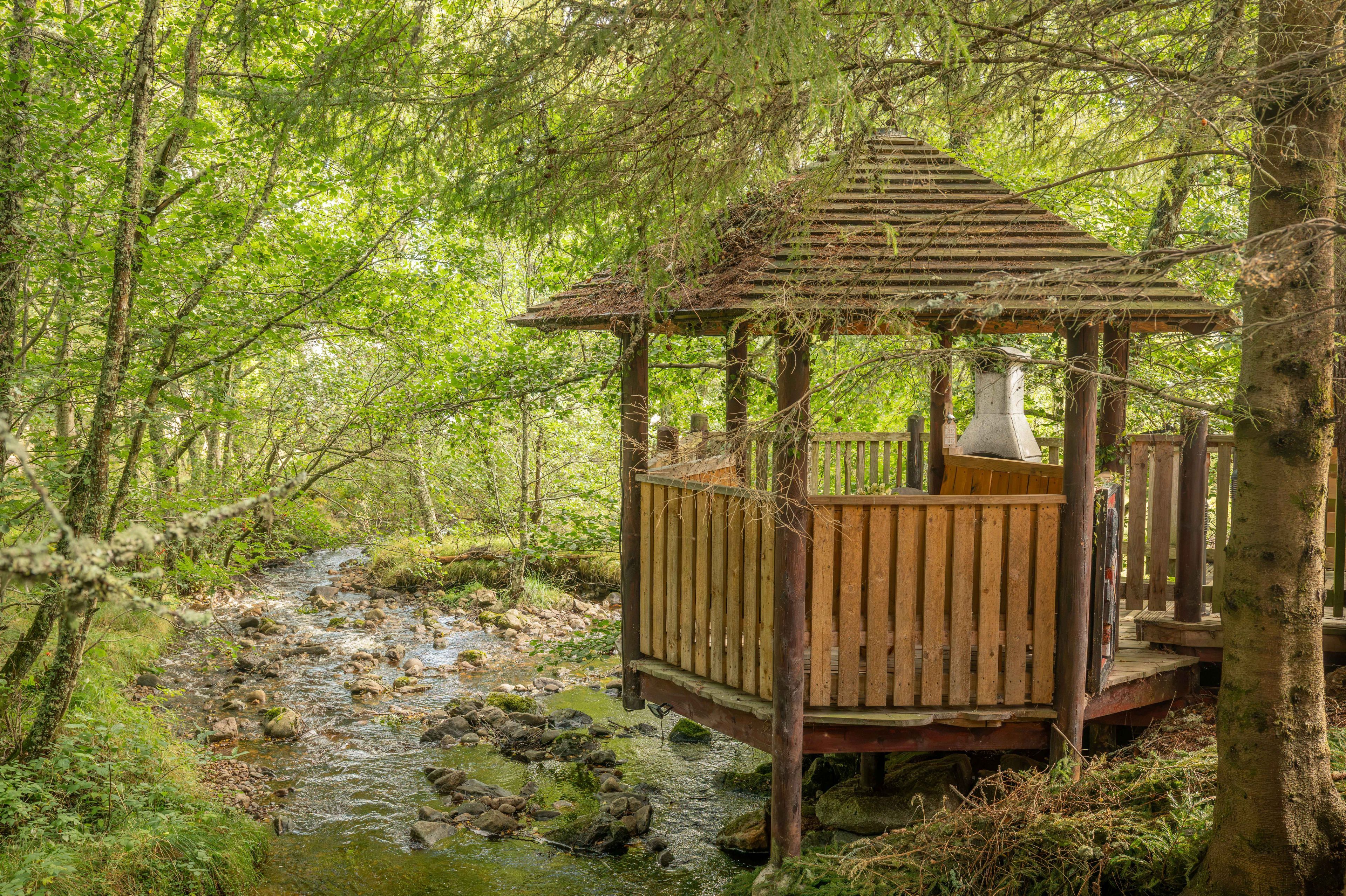 Un belvédère en bois situé dans une zone boisée, près d’un ruisseau.