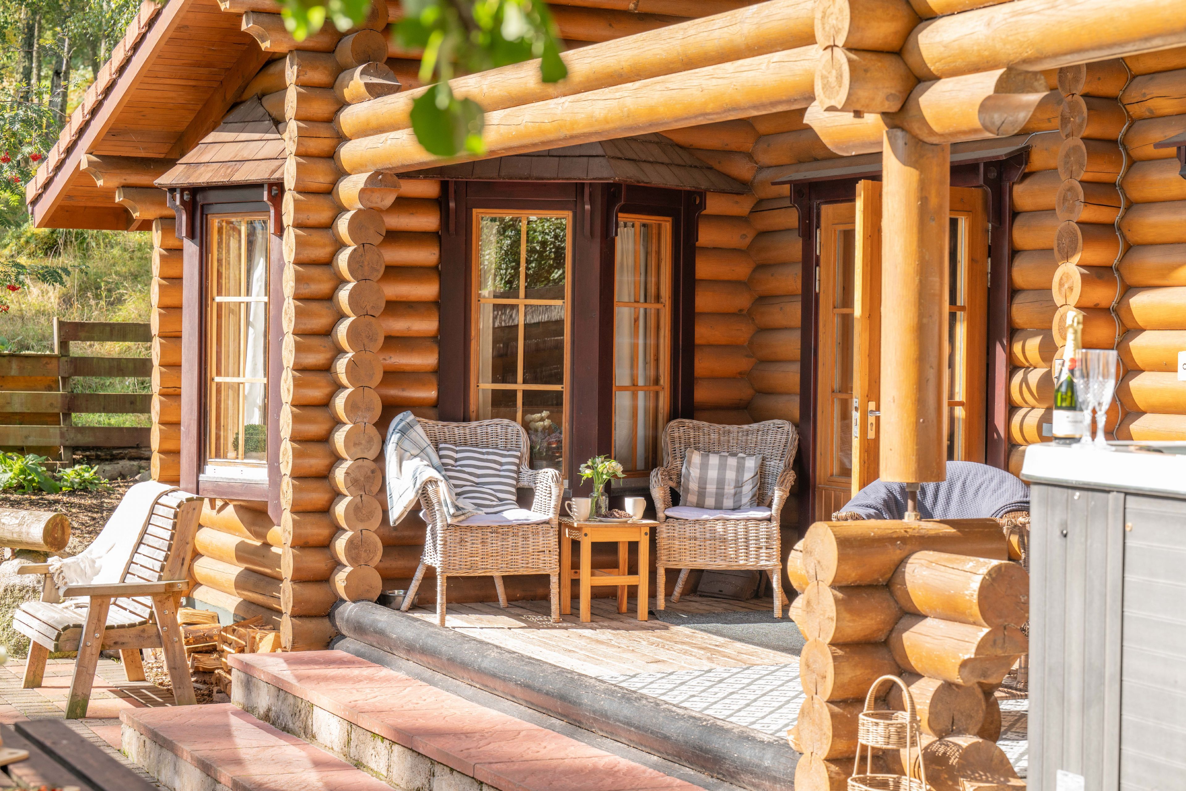 Une cabane en rondins avec une véranda, deux fauteuils en osier, une petite table et une bouteille de champagne.