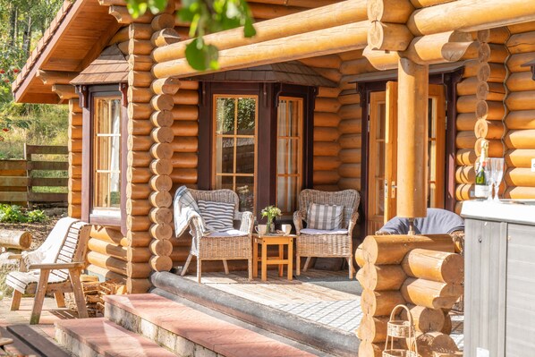 A log cabin with a porch, two wicker chairs, a small table, and a bottle of champagne.