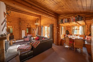 A log cabin interior with a fireplace, a sofa, a dining table set for two, and a wooden ceiling.
