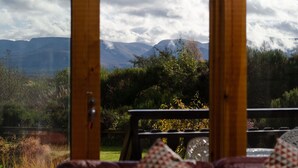 Vista desde una ventana con marco de madera, que da a un paisaje montañoso con árboles y una zona cubierta de hierba.
