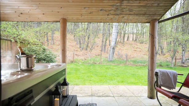 Un patio techado con techo de madera, una mesa con una botella y una olla, y un banco.